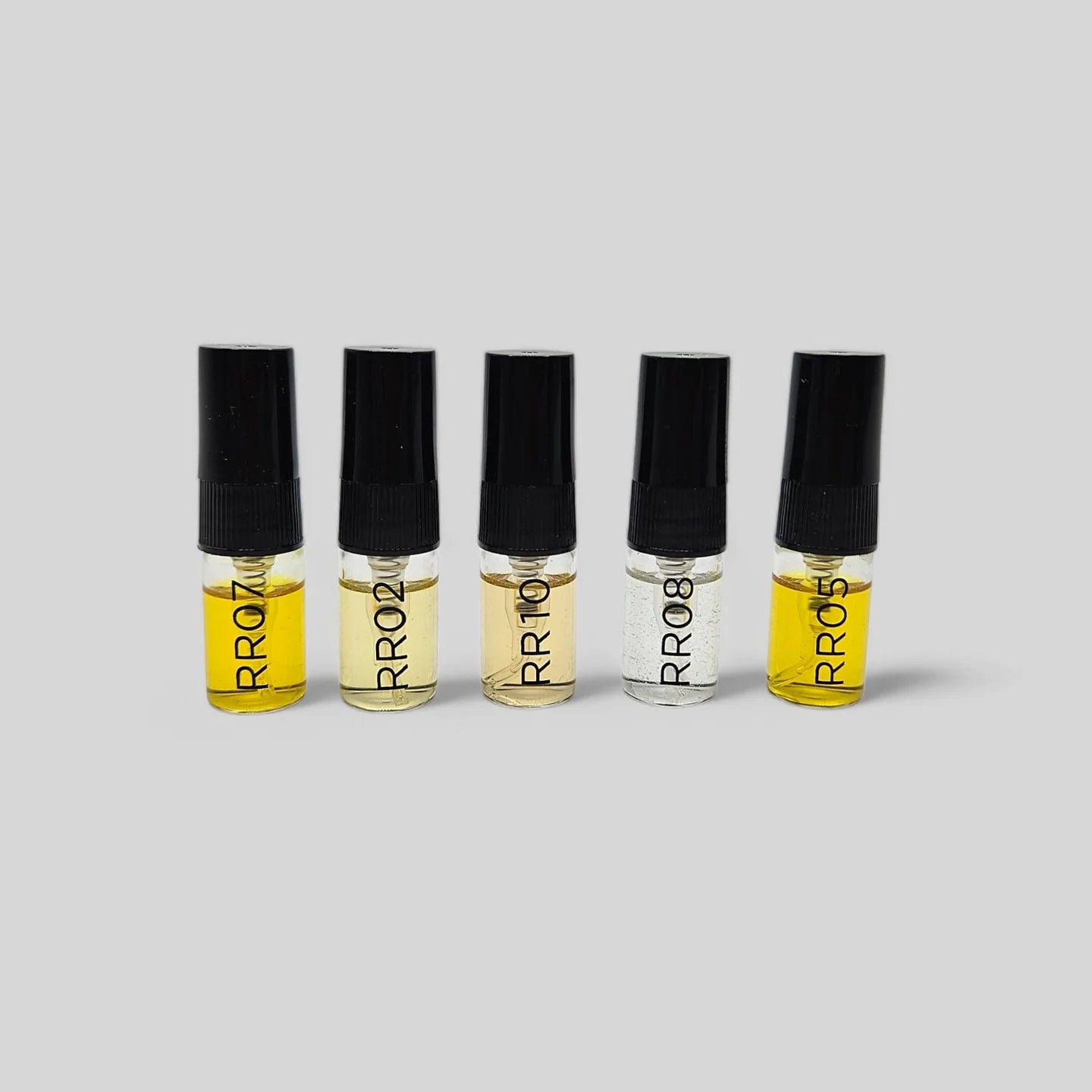 Five small glass bottles with black caps containing a yellow liquid on a gray background